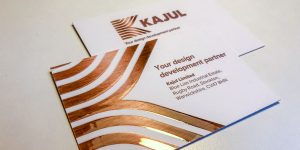 A white business card with copper geometric accents showcases KAJUL and the tagline Your design development partner. Created by Glued Limited, a leading branding agency in Warwickshire, the card includes contact details for their office on Rugby Road, Stockton.