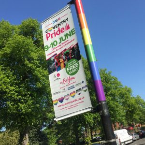 A vibrant outdoor banner for Coventry Pride 2018, designed by Glued Limited, showcases rainbow stripes and sponsor logos. Promoting a free event on June 9-10, it includes the hashtag #BeYou and website details at the bottom.